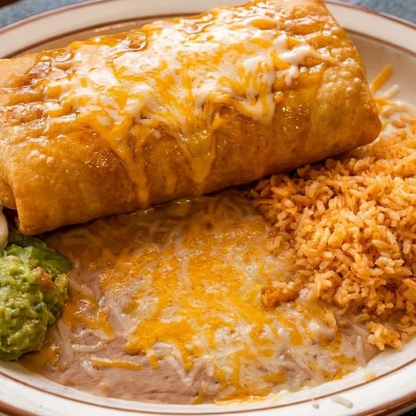 Golden-fried chimichanga covered in melted cheese, with rice, refried beans, guacamole, and sour cream.