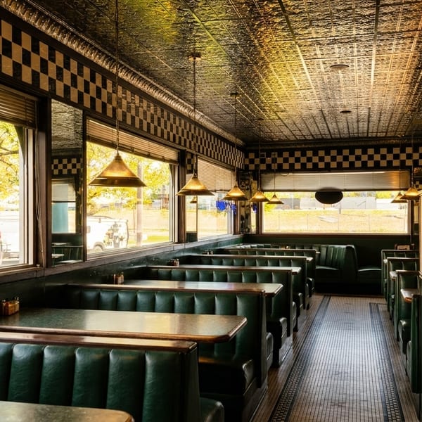 Interior of a retro diner with green booths, checkered walls, and a patterned ceiling.